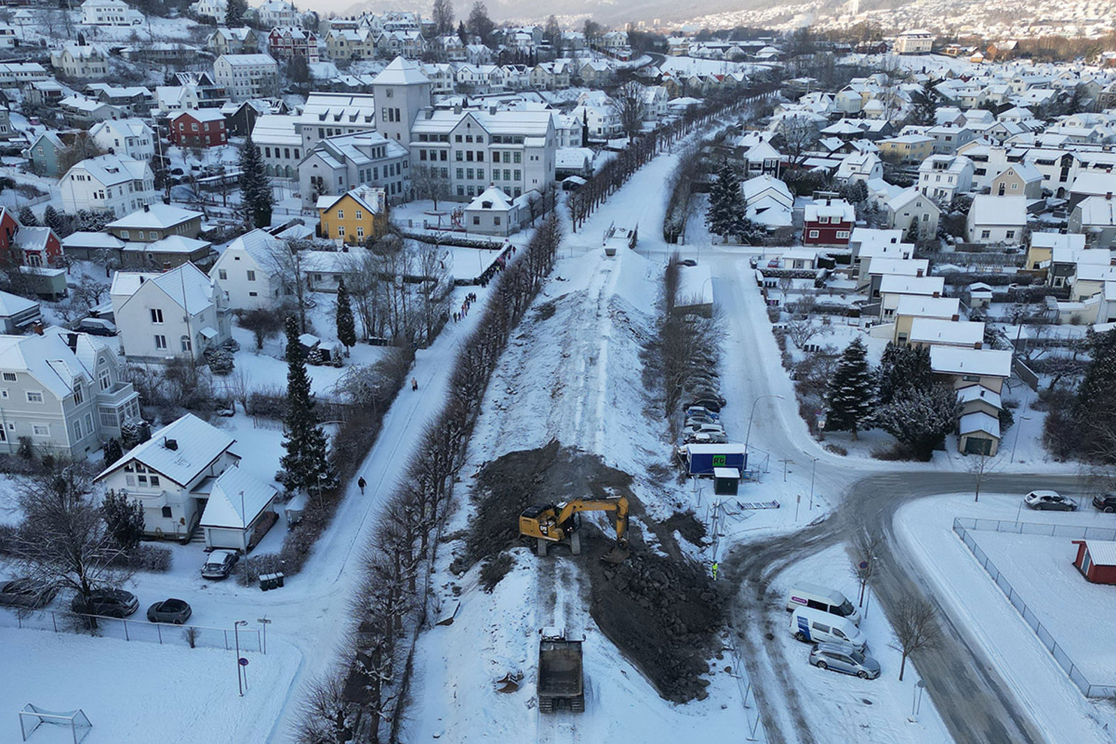 En gravemaskin står på en fylling som går gjennom et boligområde.