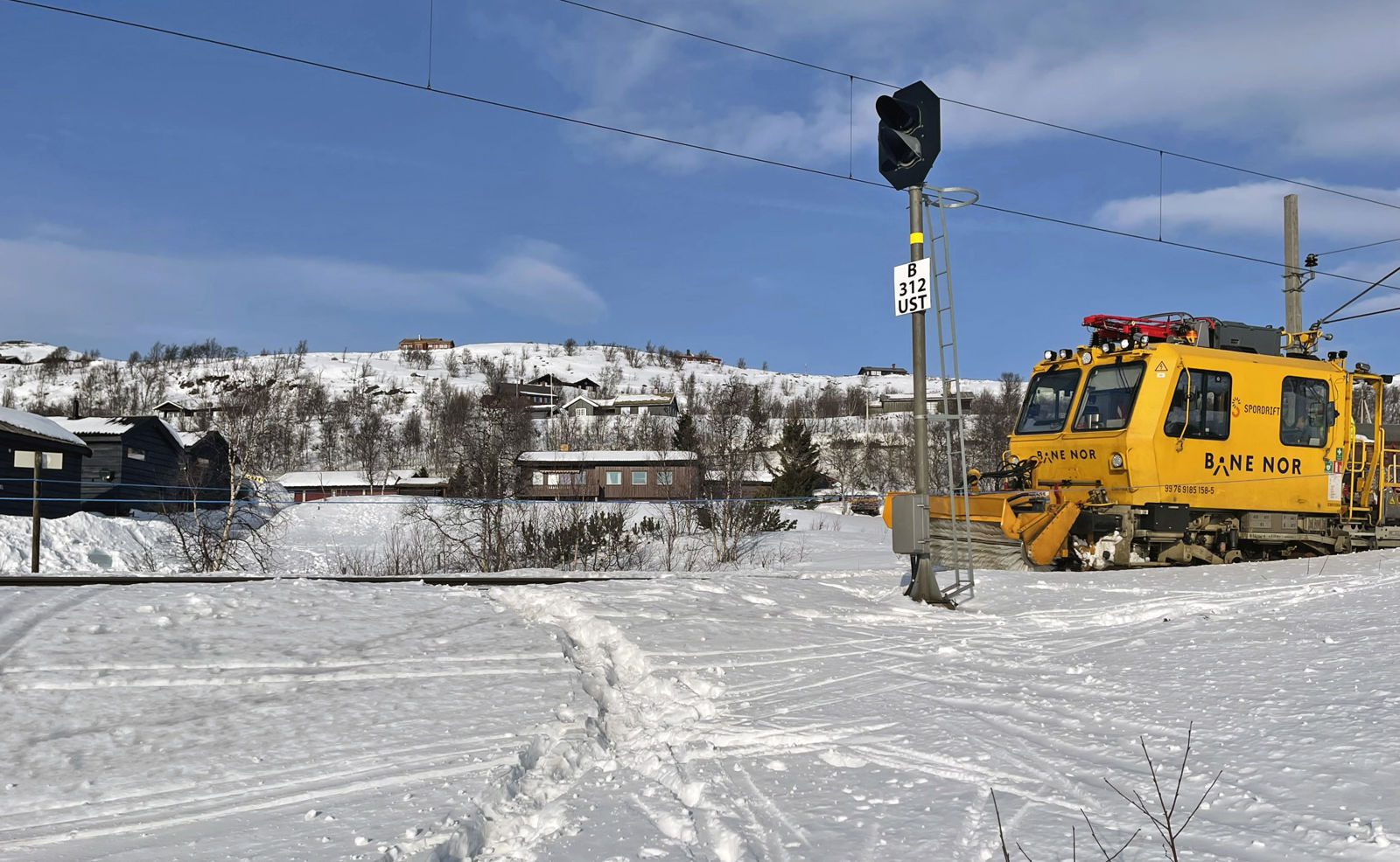 Spor i snøen krysser jernbaneskinnene. En gul arbeidsmaskin fra Bane NOR står på sporet.