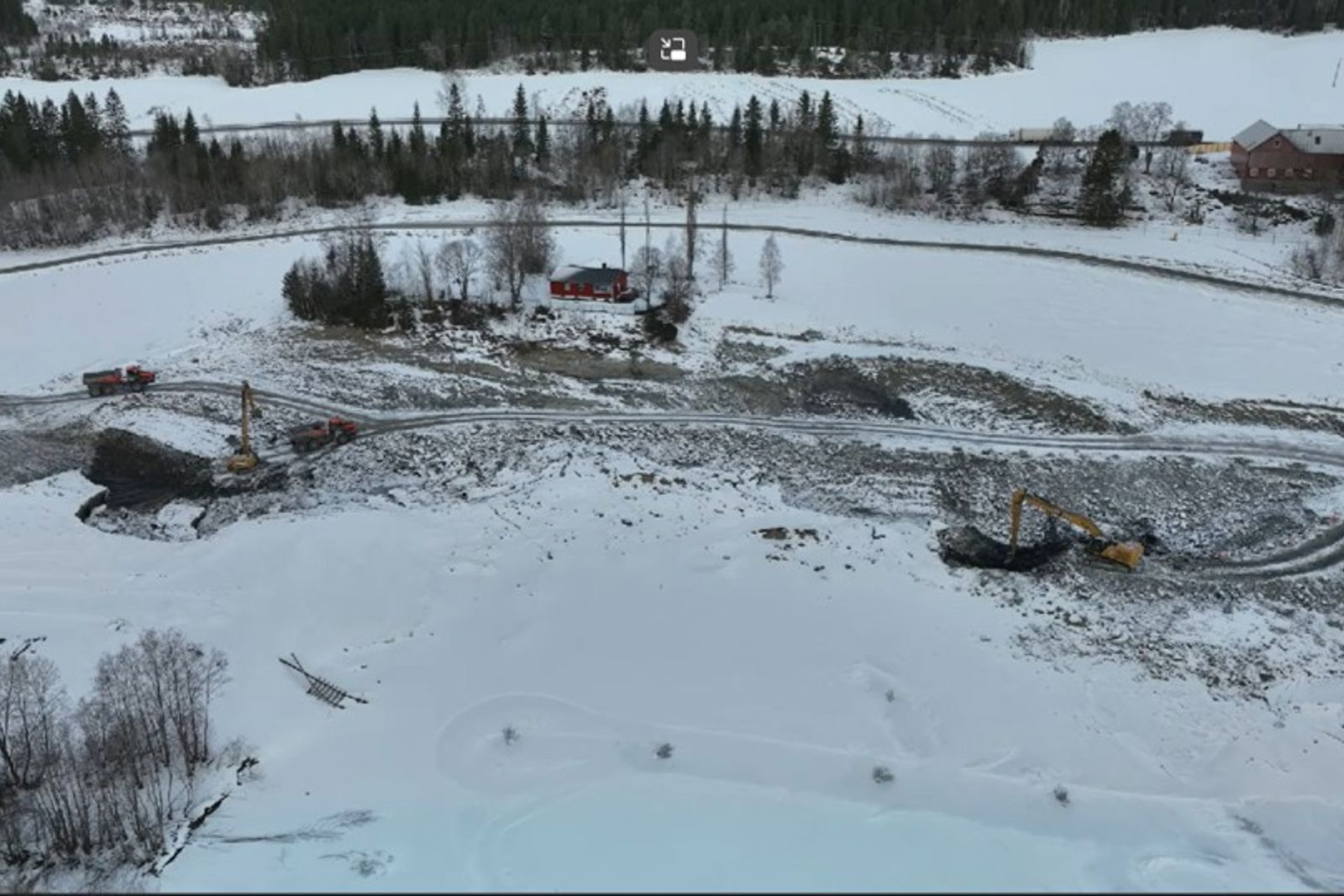 Vinterlandskap med snø over jordet + gård. Skredgropa som jevnes ut ligger under det tynne snølaget.