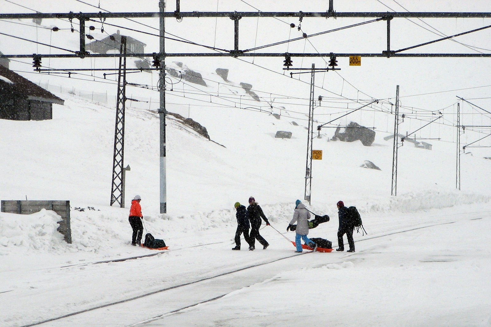 Fem personer med bagasje trekker oppakning over sporet på pulk/akebrett.