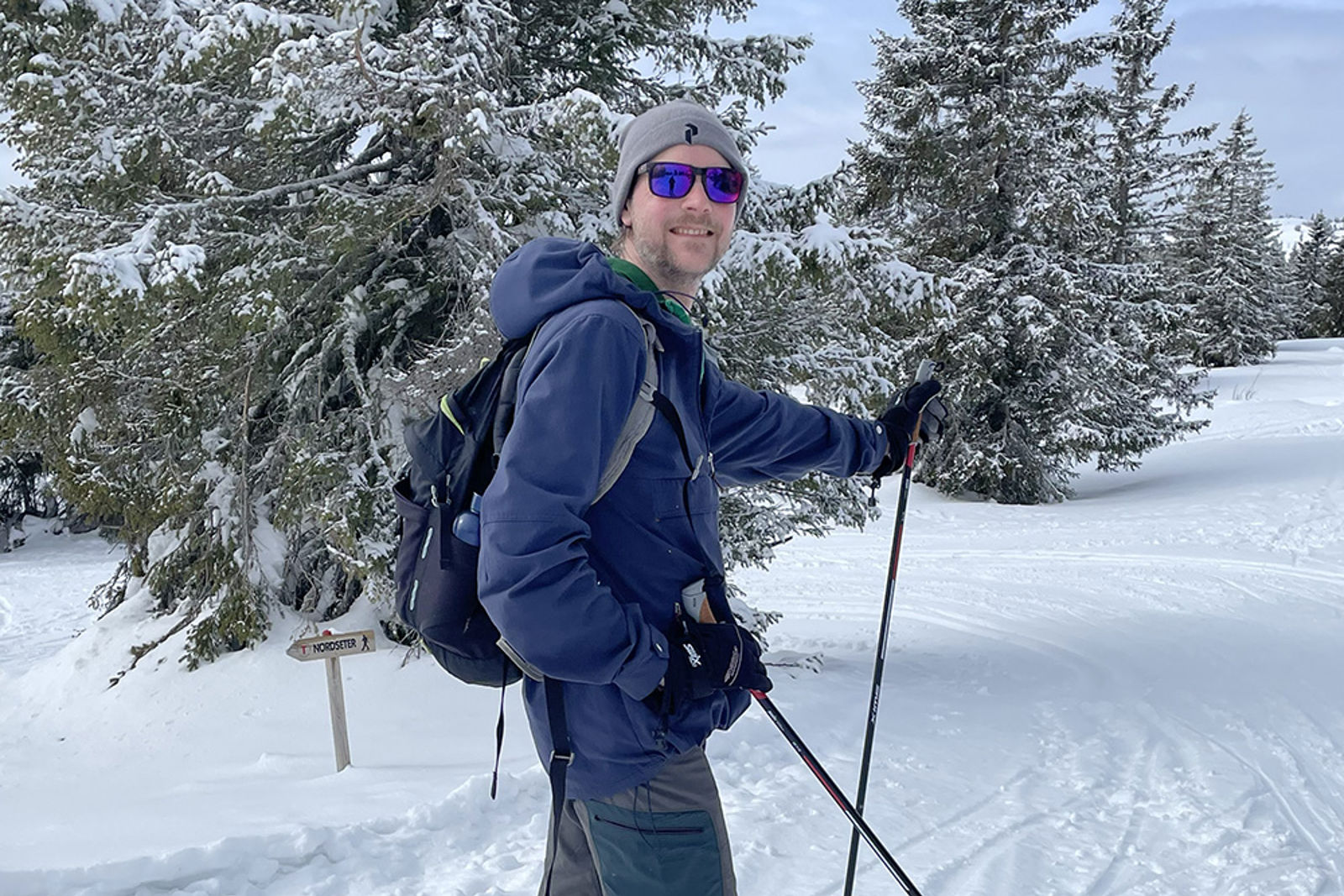 I skiløypa med turutstyr, sekk og solbriller. Snødekte trær i bakgrunnen.