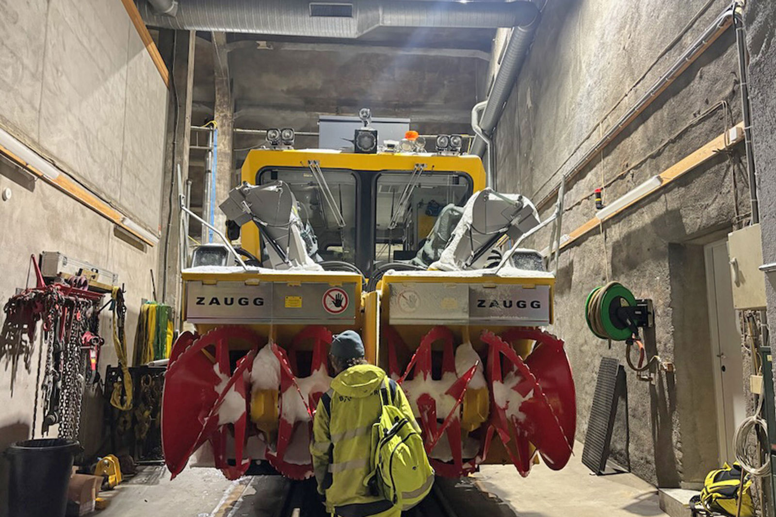 En skinnegående snøfreser parkert i lokstall. En person i forgrunnen blir liten i forhold