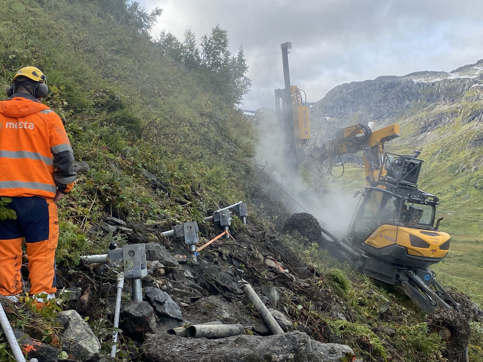 Mann og gravemaskin i bratt terreng.